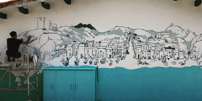L’artista Ricard Ferran està pintant un mural a la caseta de pescadors al Port d’Arenys
